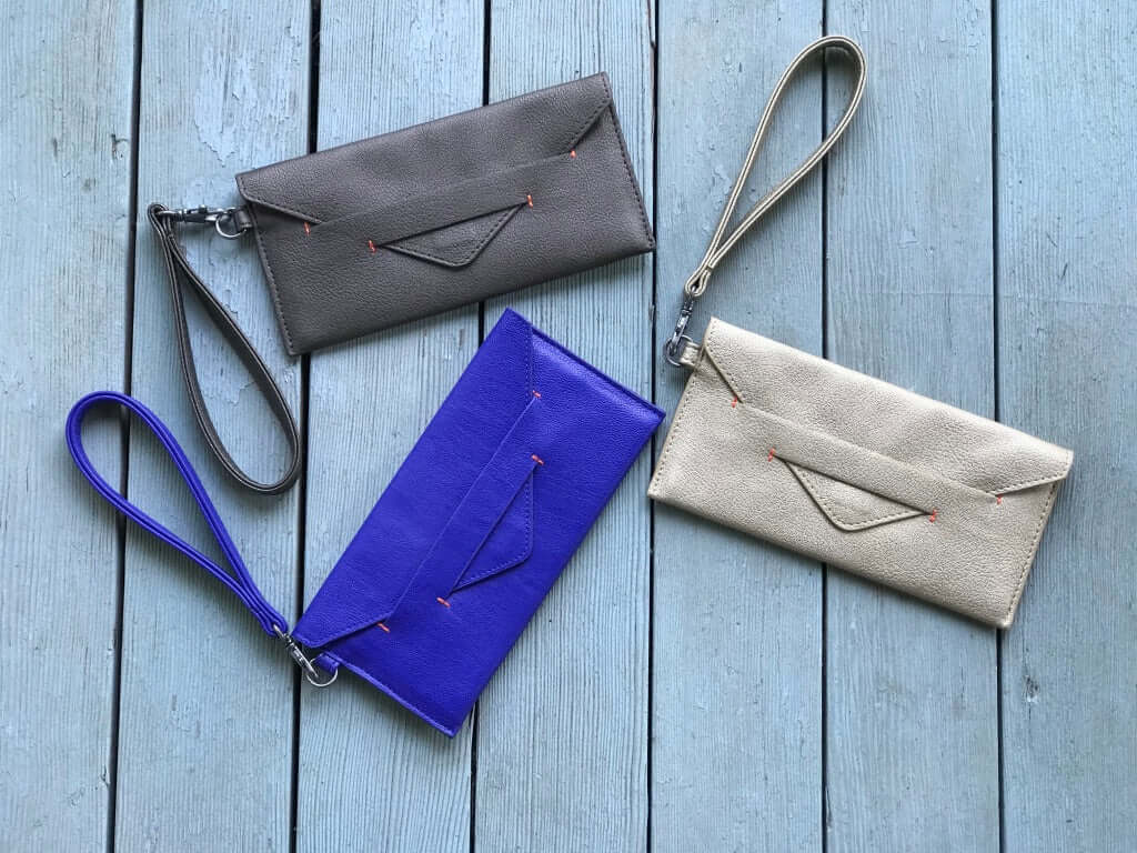 Delancey Vegan Wallet in various colors with detachable wrist straps displayed on a wooden surface