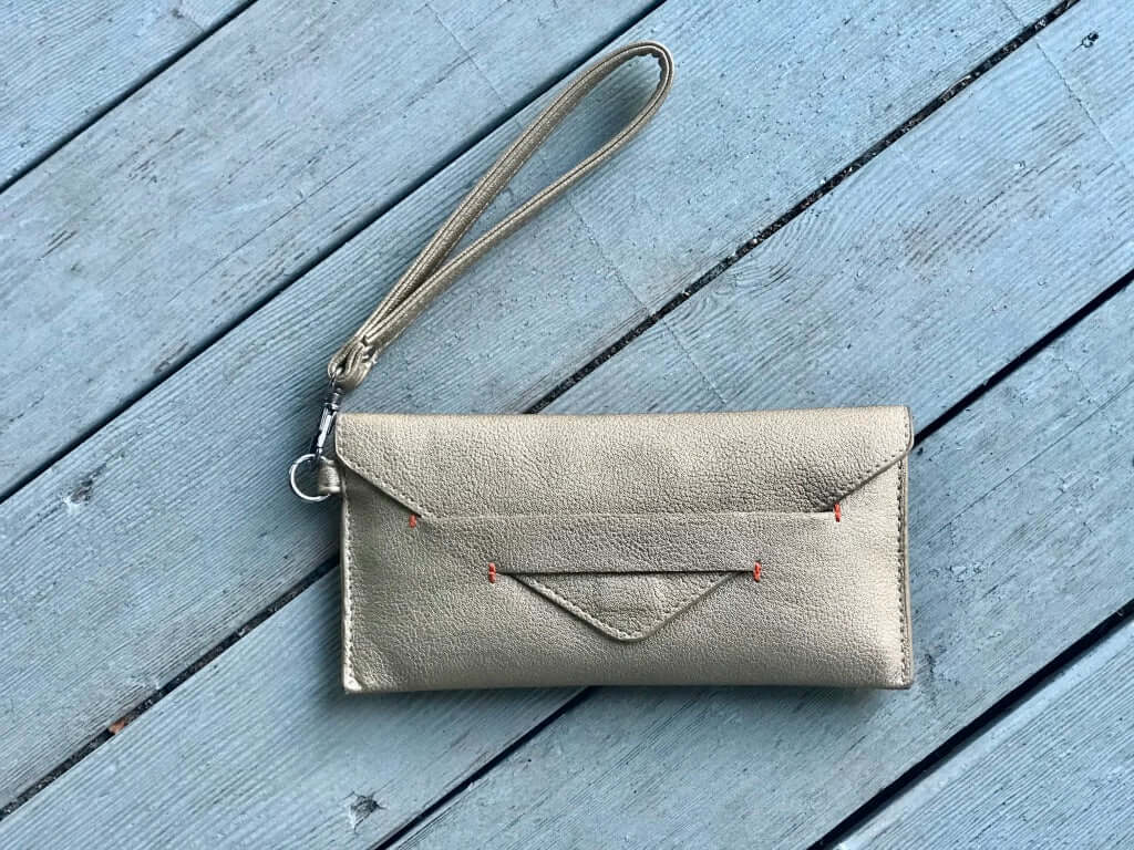 Delancey Vegan Wallet on wooden surface with detachable wrist strap and hidden magnet closure, crafted from supple vegan leather.