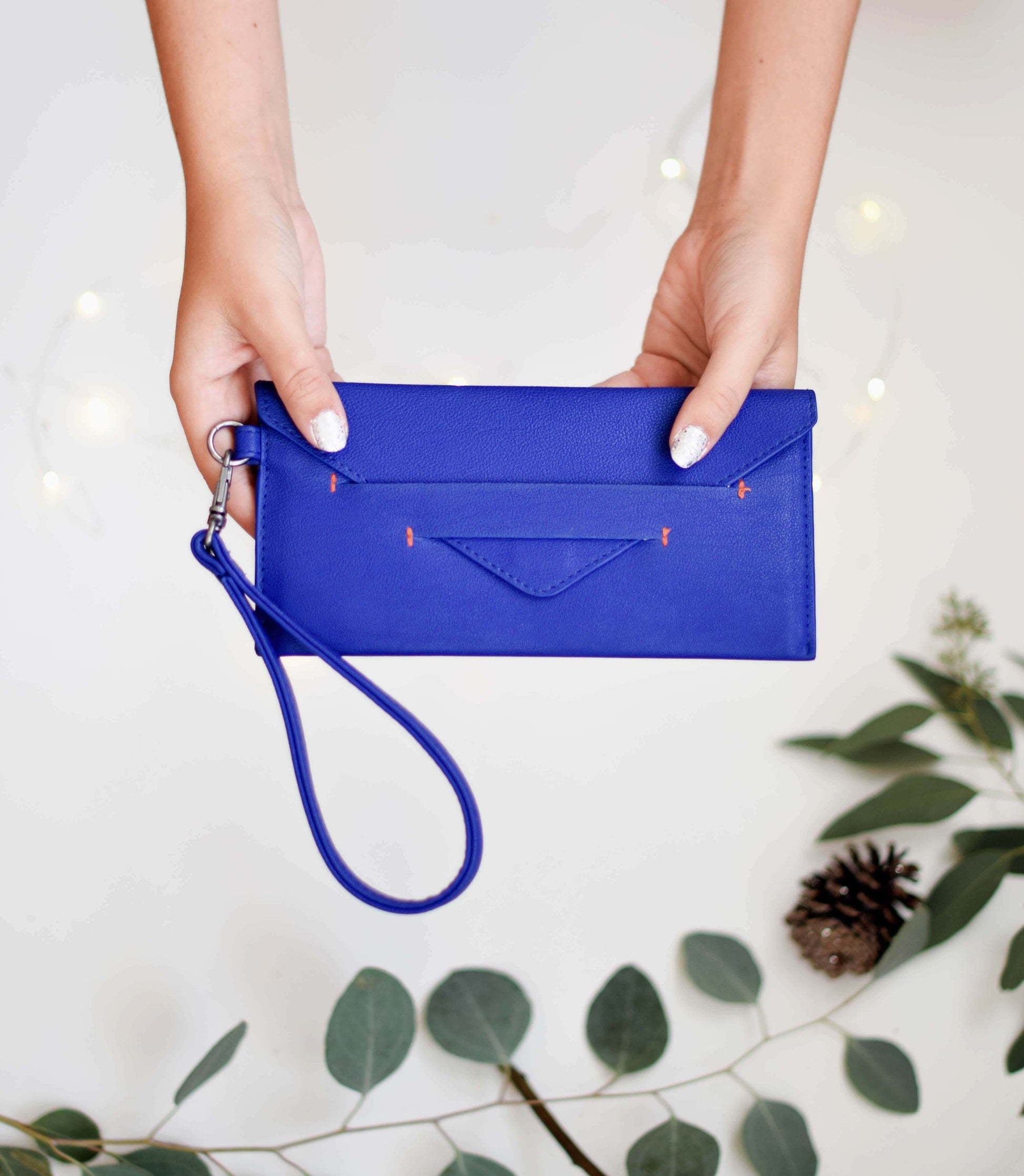 Woman holding blue Delancey Vegan Wallet with detachable wrist strap displayed against a decorative background