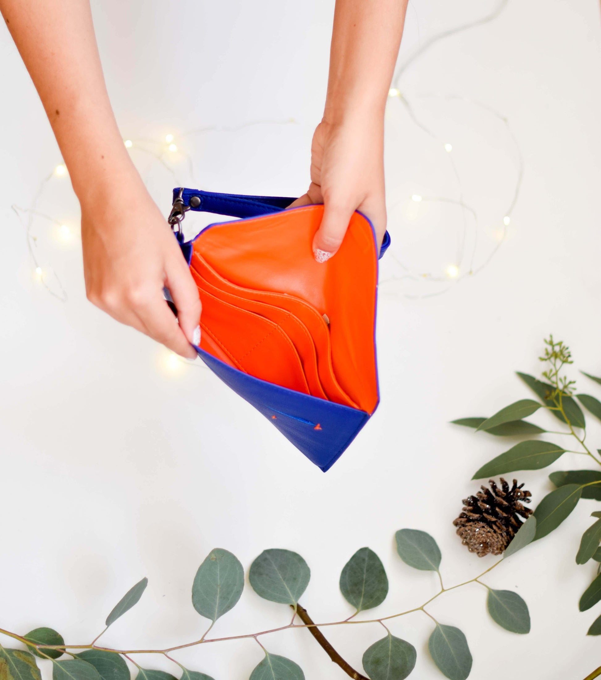 Open Delancey Vegan Wallet showing orange interior and multiple compartments held by hands with a decorative background.