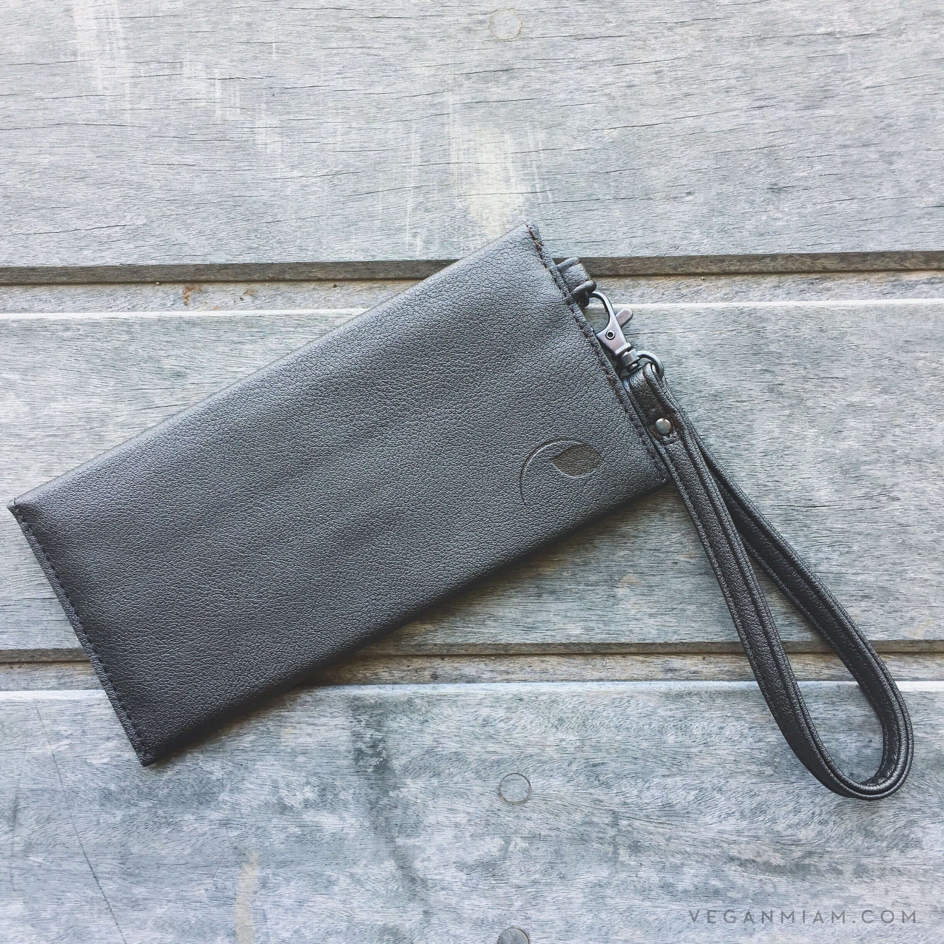 Delancey Vegan Wallet in supple vegan leather with detachable wrist strap and magnet closure on a wooden surface.